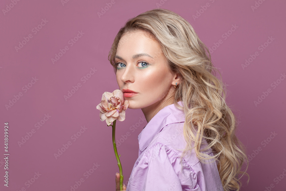 Fototapeta premium Fashion beauty portrait of pretty woman with healthy skin holding flowers near her face on bright pink background, studio portrait