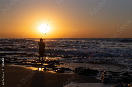 Fisherman at sunrise silhouette on the edge of the ocean