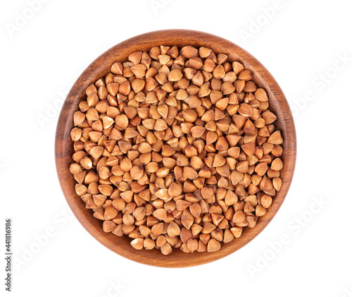 Roasted buckwheat grains in wooden bowl, isolated on white background. Dry brown buckwheat groats. Top view.