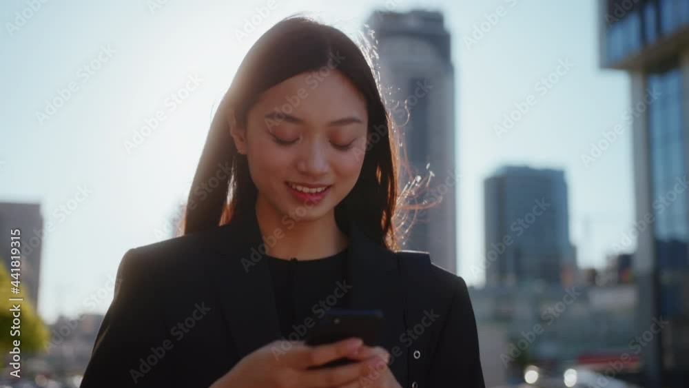 Beautiful mixed-race young girl using mobile phone for typing messages, walking in city center, admiring sunset and street views. Urban people. Business women.