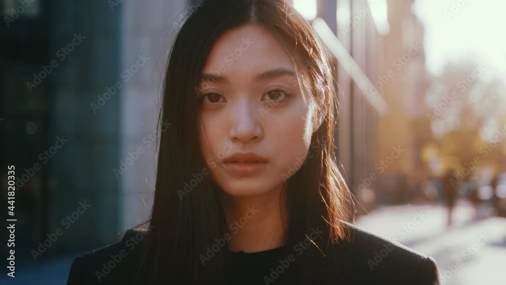 Portrait of nice mixed-race asian young beautiful woman with straight black hair posing to camera outside. Urban people, cityscape, sunlight. Females.