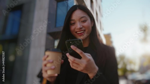 Joyful young asian business girl using mobile phone networking with online friends typing messages drinking coffee outside. Beautiful people. City life.
