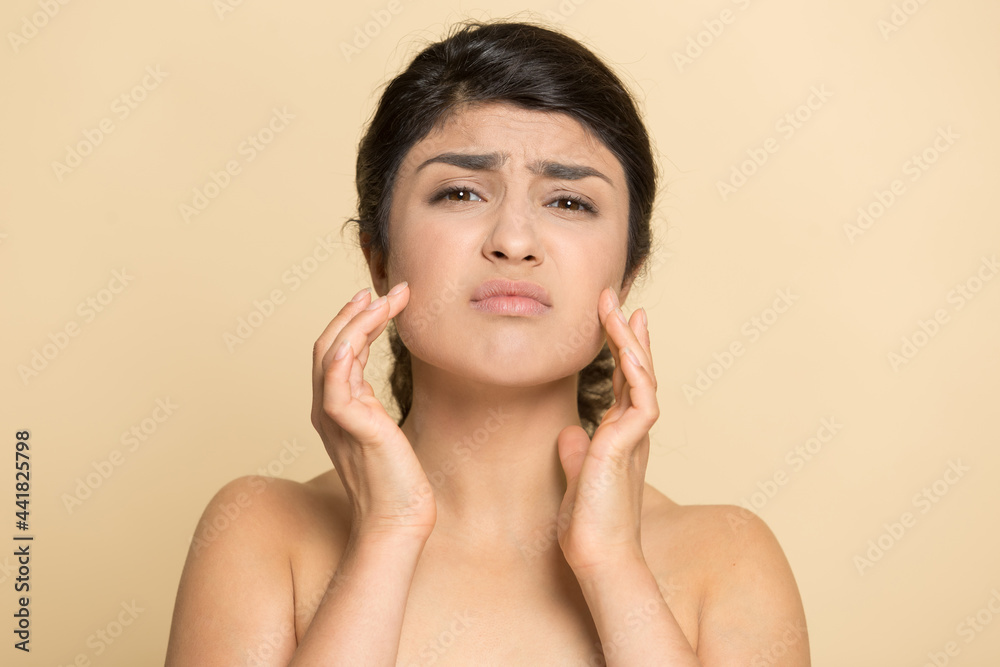 Portrait of unhappy young Indian woman isolated on yellow studio background touch face worry about pimples wrinkles. Upset mixed race female think of botox treatment. Facial skincare concept. Portrait of unhappy young Indian woman isolated on yellow studio background touch face worry about pimples wrinkles. Upset mixed race female think of botox treatment. Facial skincare concept.