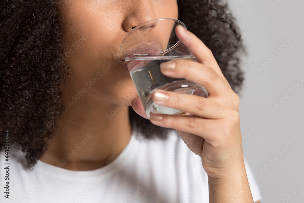Crop close up of thirsty African American woman hold glass drink pure mineral clean still water for body refreshment. Dehydrated mixed race female enjoy aqua follow healthy lifestyle. Diet concept. Crop close up of thirsty African American woman hold glass drink pure mineral clean still water for body refreshment. Dehydrated mixed race female enjoy aqua follow healthy lifestyle. Diet concept.