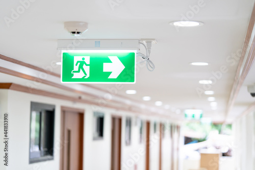Fotografia A Arrow light box sign of EMERGENCY FIRE EXIT is hung on the ceiling in hospital walkway, Idea for event fire or evacuation drills