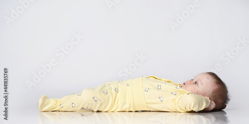 Baby lying on his back, happy infant wearing a yellow bodysuit jumpsuit, beautiful baby lying on a white background, looking up