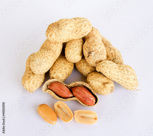 Peanuts stacked separately on a white background . Two kernels have already been removed. One of the peanuts unpacked reveals a red seed on the side.