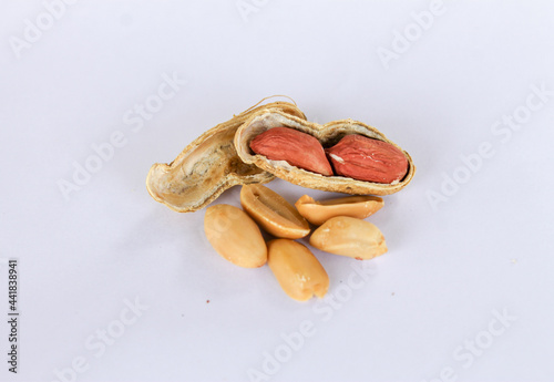 Peanuts piled up separately on a white background . One has been peeled off to reveal a red seed inside. There are two seeds that have been carved apart in front.