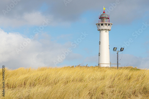 The J.C.J. van Speijk Lighthouse with european marram grass (beach grass) under blue sky, Located on Dutch north sea coastline in Egmond aan Zee, Municipality of Bergen, North Holland, Netherlands.