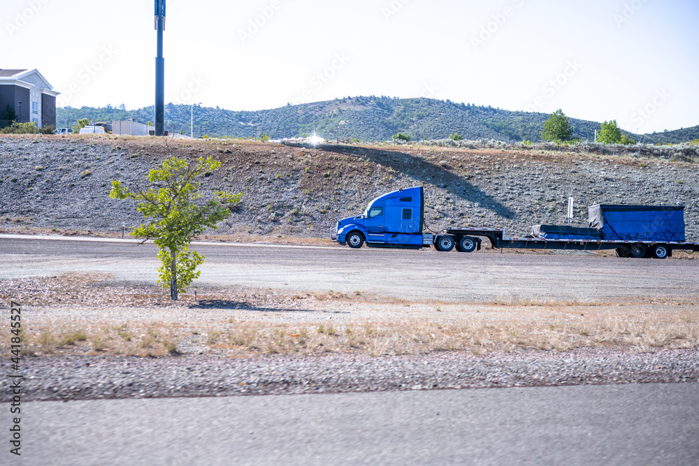 Blue big rig semi truck with loaded step down semi trailer going on the ...