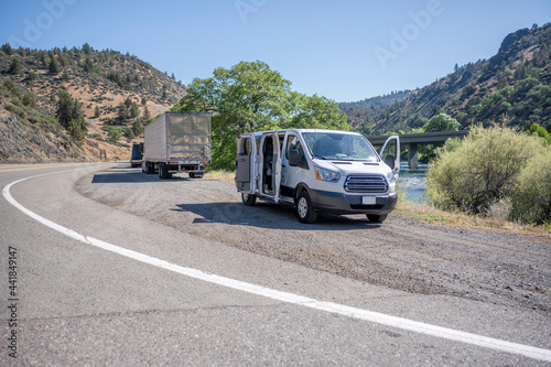 Compact mini van and big rig semi trucks with semi trailers take a break standing on the road shoulder on the bank of a mountain river © vit