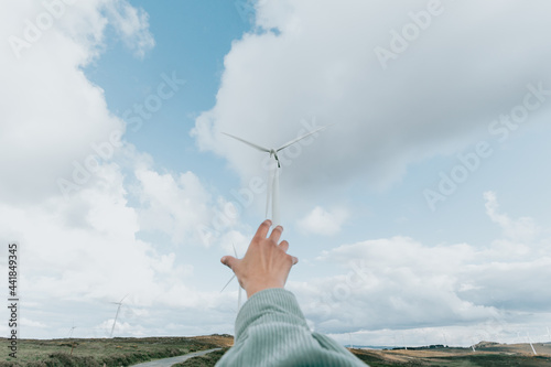 Fototapeta Naklejka Na Ścianę i Meble -  Human hand reaching Wind Turbines Windmill Energy on the nature, during a super sunny day, with copy space and a lot of air