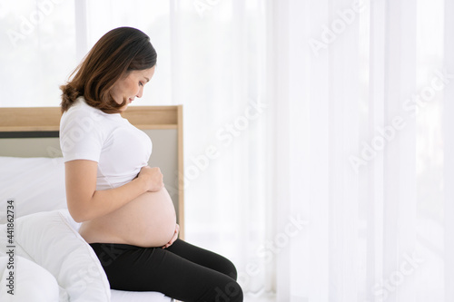 Free Download Asian beautiful and happy woman in pregnancy sitting beside the bed in bedroom.  - GFXLoad