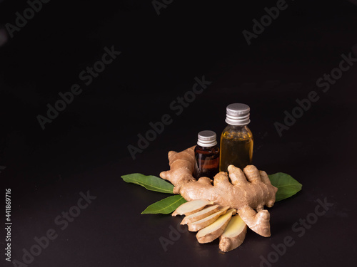 Ginger essential oil with sliced ginger on black wooden background