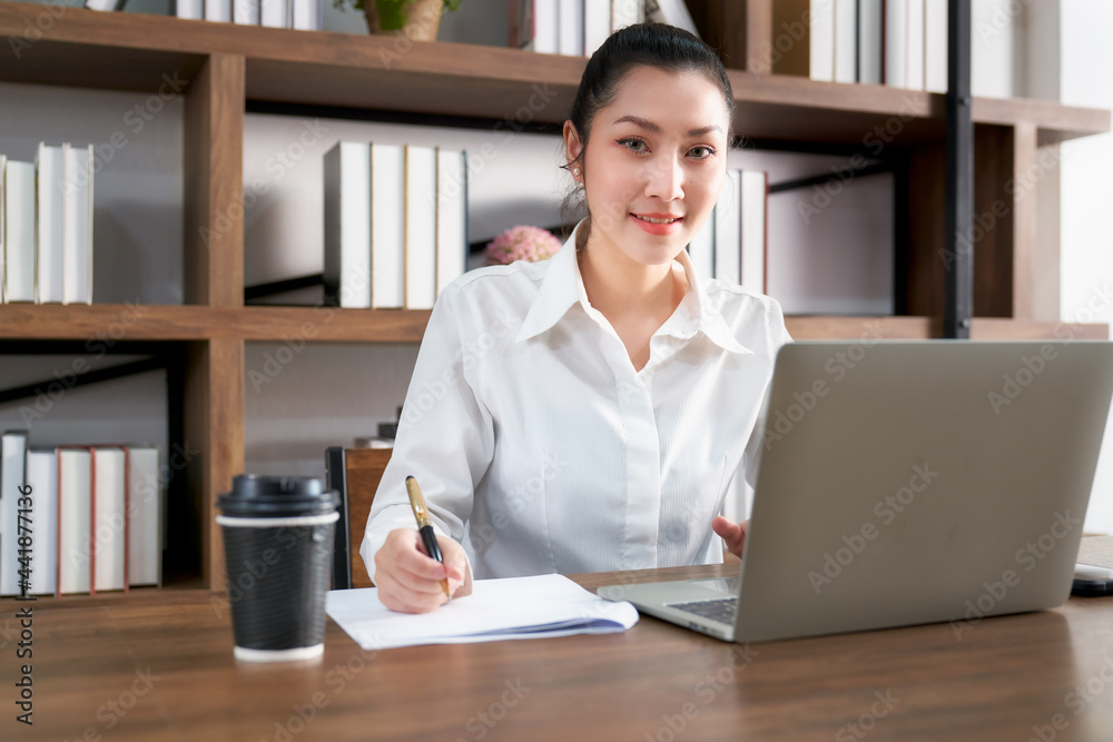 Asian beautiful businesswoman smiling and working with laptop and coffee cup in co working space Asian beautiful businesswoman smiling and working with laptop and coffee cup in co working space
