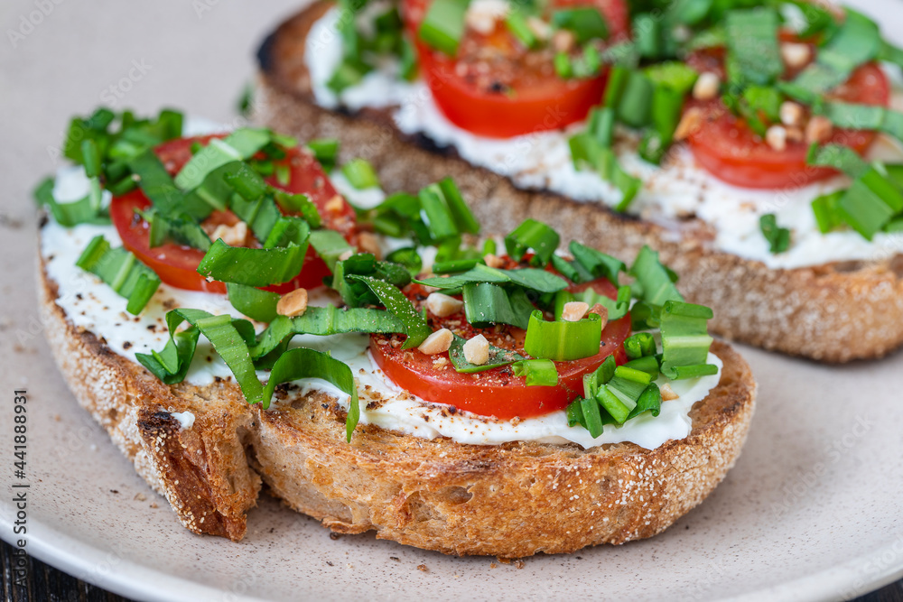 Delicious toasted bread with white cream cheese, green wild garlic and tomato on plate, close up Delicious toasted bread with white cream cheese, green wild garlic and tomato on plate, close up