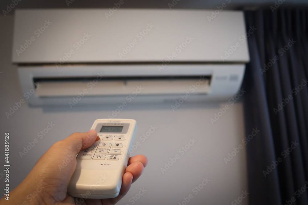 Air conditioner inside the room with close up man hand holding using directed operating remote controller. Air conditioner inside the room with close up man hand holding using directed operating remote controller.