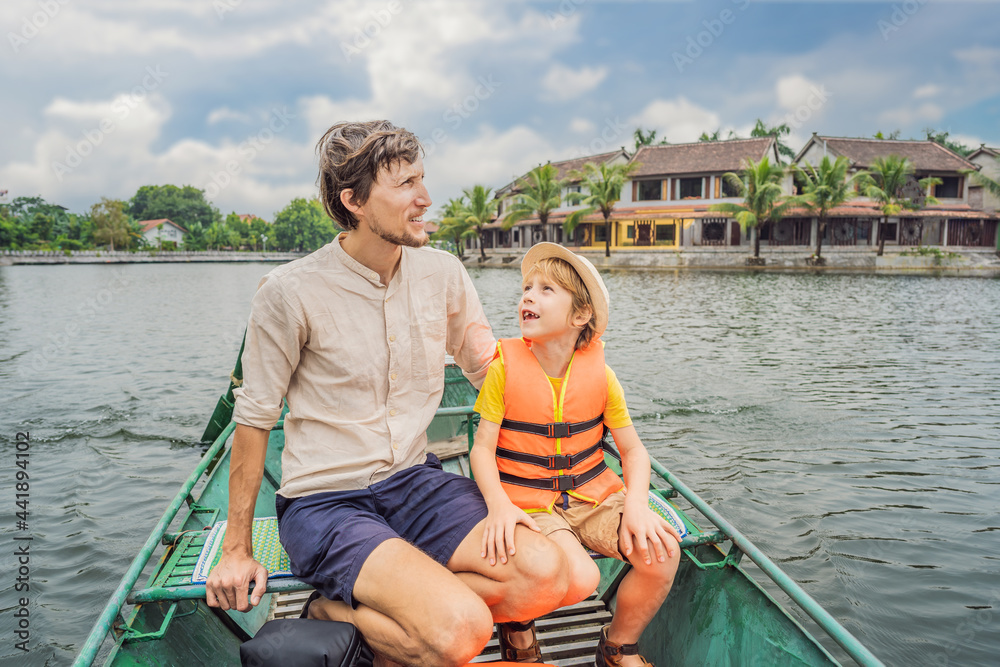 Fototapeta premium Dad and son tourists in boat on the lake Tam Coc, Ninh Binh, Viet nam. It's is UNESCO World Heritage Site, renowned for its boat cave tours. It's Halong Bay on land of Vietnam. Vietnam reopens borders
