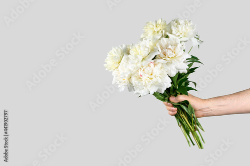 Male hand holds beautiful bouquet of white peonies. Flower delivery concept