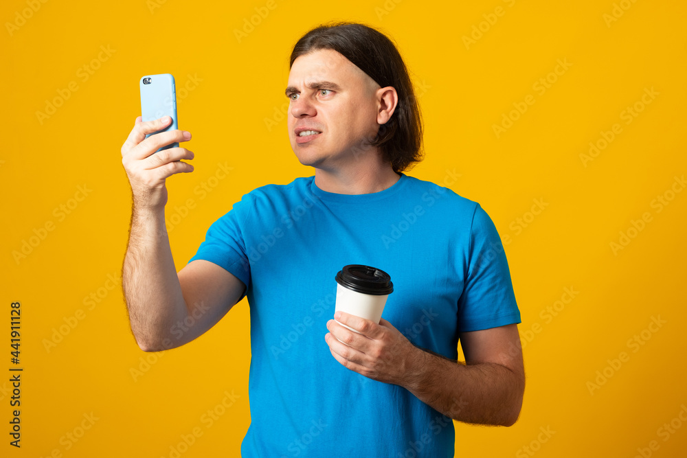 Handsome guy with funny expression, chats in cellphone, reads strange received message, drinks hot beverage from disposable cup, connected to wireless internet, dressed in casual wear. Handsome guy with funny expression, chats in cellphone, reads strange received message, drinks hot beverage from disposable cup, connected to wireless internet, dressed in casual wear.