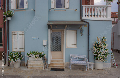 Detail of a typical fisherman's house. Blue house with white balconies and terrace. White flowers in the vases. Rustic bench near the door.