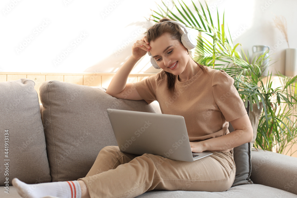 Smiling young woman with headphones and laptop on the sofa. Smiling young woman with headphones and laptop on the sofa.