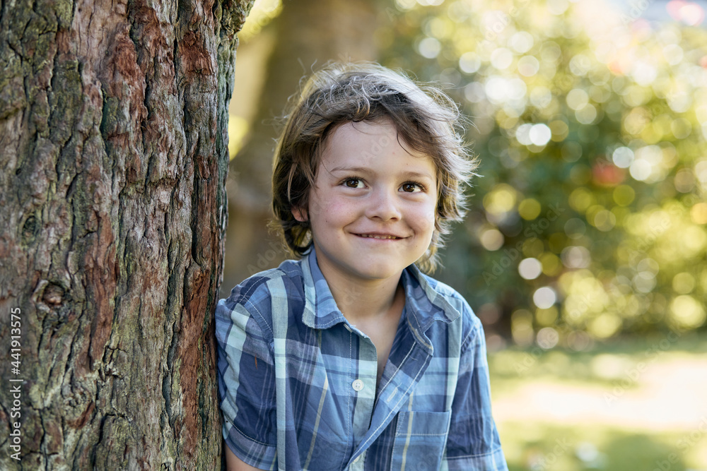 Cheerful kid leaning on tree while chilling in park Cheerful kid leaning on tree while chilling in park