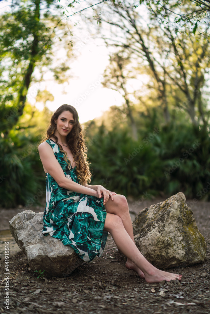 Beautiful woman sitting on stone in lush forest Beautiful woman sitting on stone in lush forest