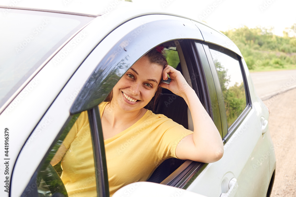 Smiling woman sitting behind the wheel of her car, parked on the side of the road.