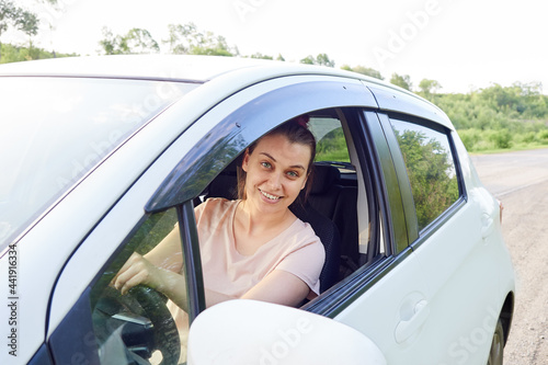smiling woman driver is sitting in her car, window is open, woman is looking at camera