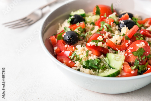 Bowl with couscous and vegetables on light background, closeup