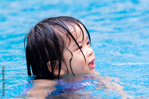 Happy Asian child girl sweet smiling in the blue pool. Head shot of kid playing water in the summer time. Children aged 4 - 5 years old.