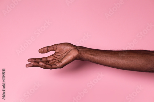 Hand of anonymous black man with palm upwards against pink background photo