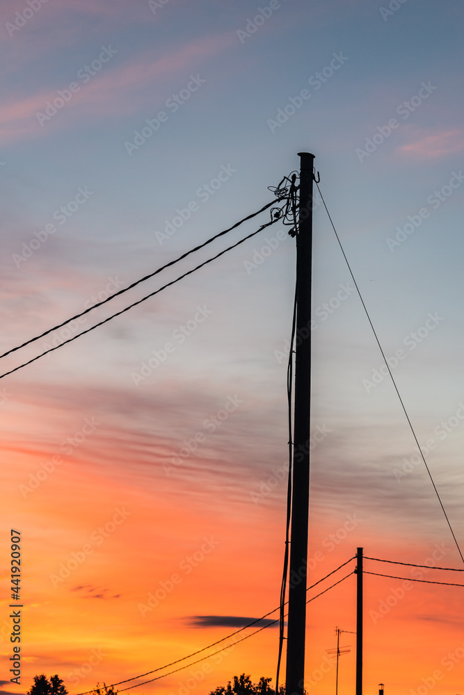 Silhouettes of electric poles and wires at summer sunset.