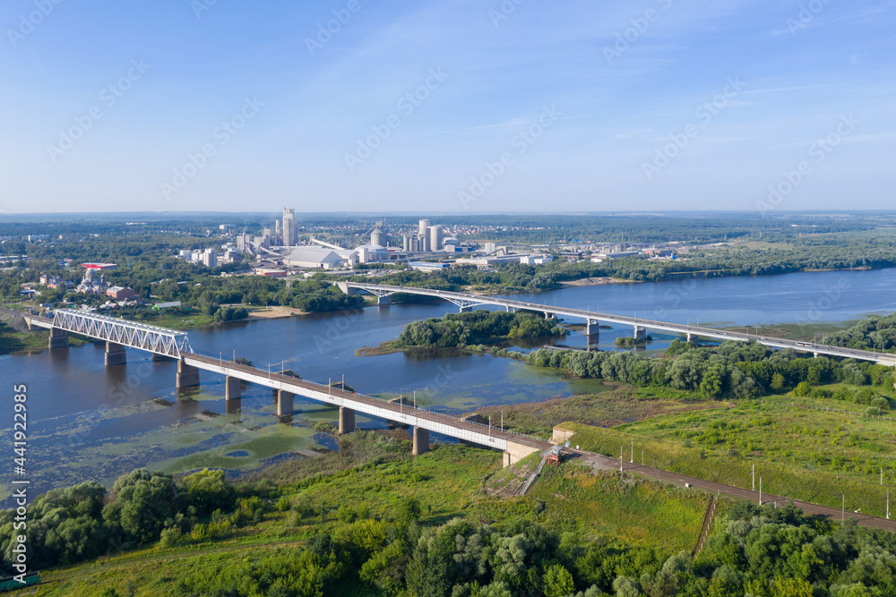 Aerial view of Oka river, bridges and Shchurovsky cement plant Holcim at sunny day. Kolomna, Moscow Oblast, Russia.
