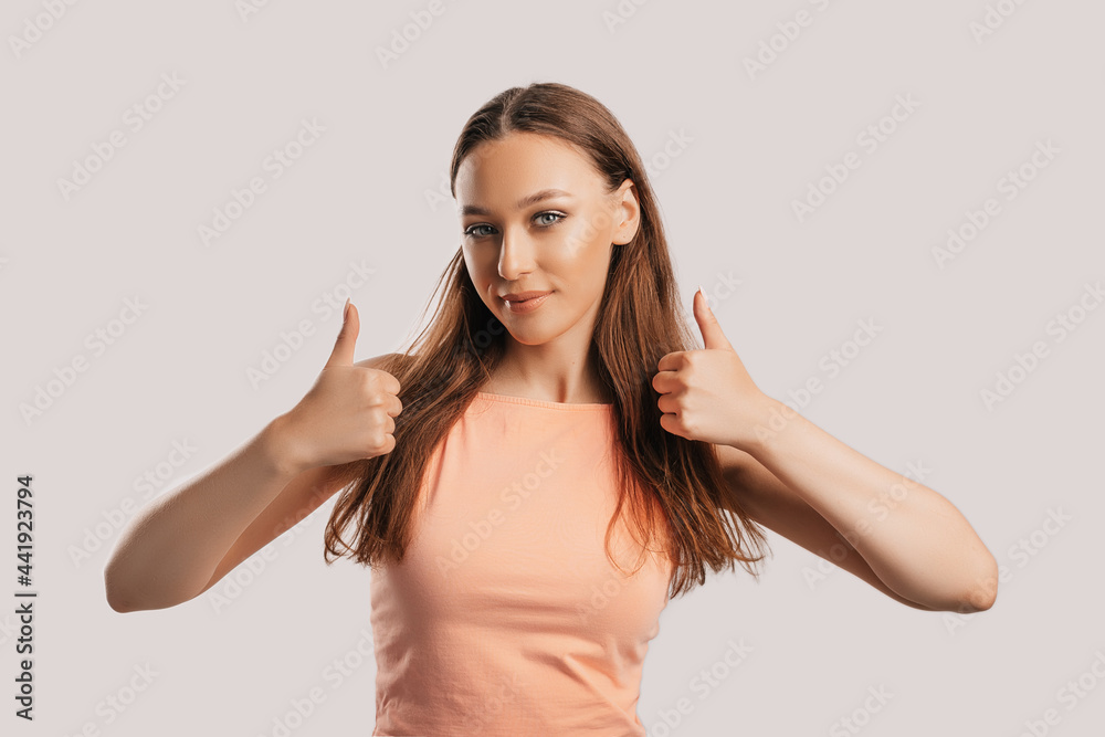 Beautiful young girl smiling and shows thumbs up gesture with two hands on a white isolated background. Positive woman points to an idea, a place for advertising Beautiful young girl smiling and shows thumbs up gesture with two hands on a white isolated background. Positive woman points to an idea, a place for advertising