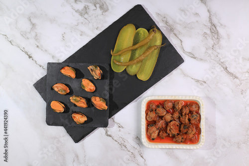 Portion of pickled mussels on a slate plate garnished with gherkin and piparras photo