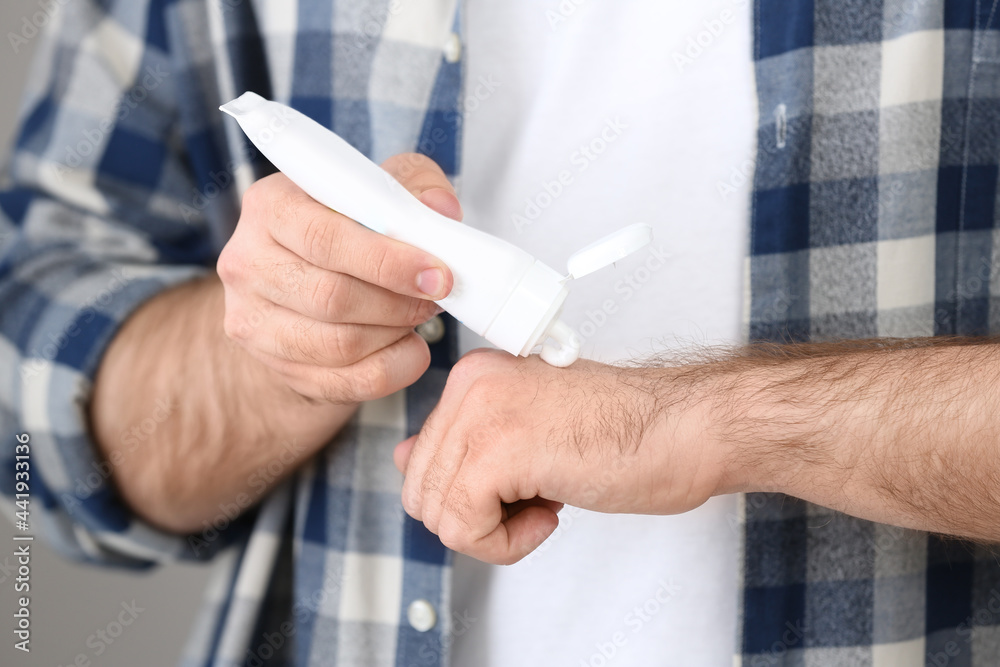 Man applying cream from tube onto hand on light grey background, closeup Man applying cream from tube onto hand on light grey background, closeup