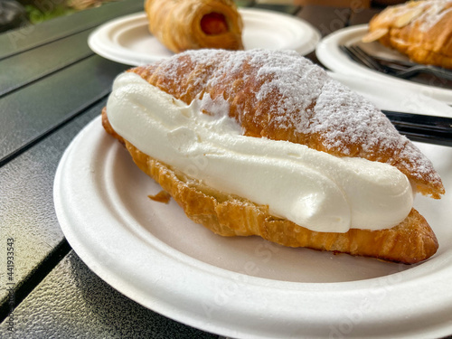 Croissant with icy sugar and cream as topping put on white paper plate in a coffee cafe