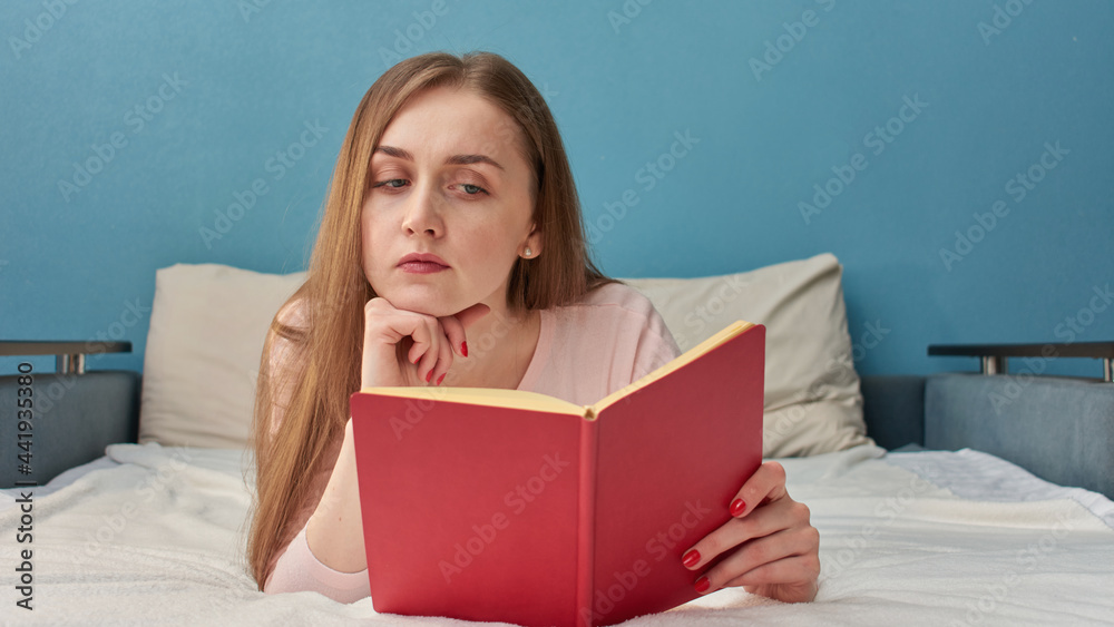 Angry young woman reading a book lying in her bedroom, portrait, 16: 9 Angry young woman reading a book lying in her bedroom, portrait, 16: 9