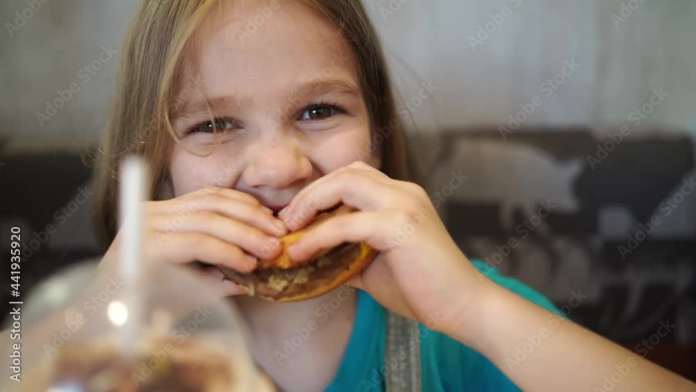 Funny kid girl eats a delicious burger in a cafe. food for children in ...