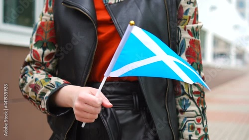 Unrecognizable woman holding Scottish flag. Girl walking down street with national flag of Scotland