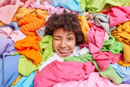 Wallpaper Mural Positive funny Afro American woman surrounded by colorful used clothes collected for recycling or donationn cleans ut her wardrobe keeps head through pile of multicolored garments shows tongue Torontodigital.ca