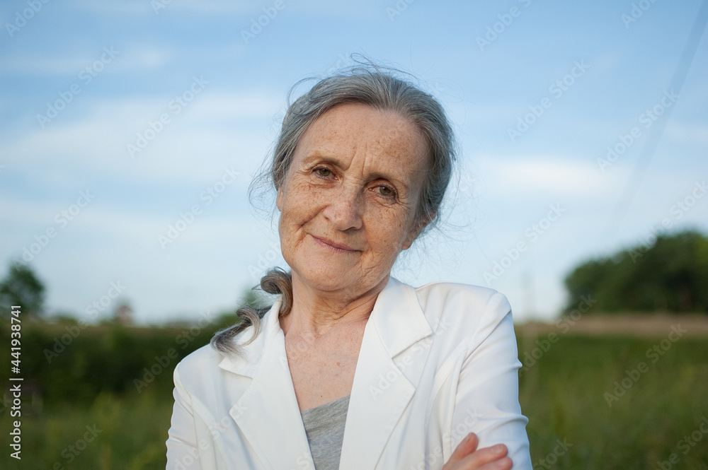 Portrait of senior woman with grey hair and face with wrinkles wearing white jacket and relaxing at park during sunny day Portrait of senior woman with grey hair and face with wrinkles wearing white jacket and relaxing at park during sunny day