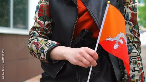 Unrecognizable woman holding Bhutanese flag. Girl walking down street with national flag of Bhutan