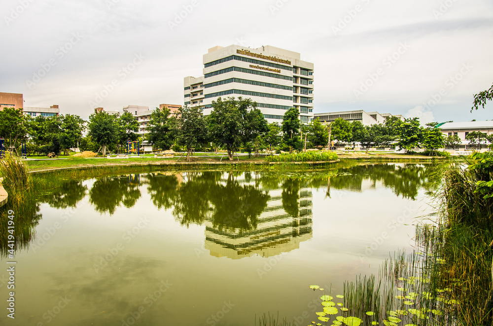 A large building with a park in front. There is a pond that reflects the image of the buildings in the water surface.