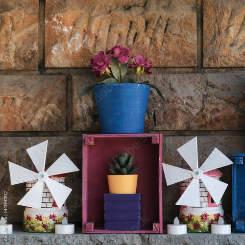 Vertical shot of plants on a pot with decorative windmills and plastic candles against brick wal photo