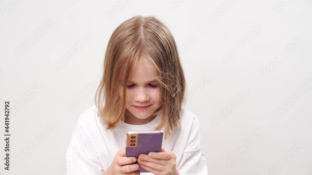 Little girl reads the message on the phone at the white wall. mobile Internet and communication to communicate with distant relatives and friends. Little girl reads the message on the phone at the white wall. mobile Internet and communication to communicate with distant relatives and friends.