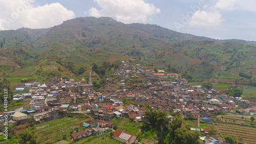 asian town with mosque in mountains among agricultural land  rice terraces. mountains with farmlands  rice fields  village  fields with crops  trees. Aerial view farm lands on mountainside. tropical