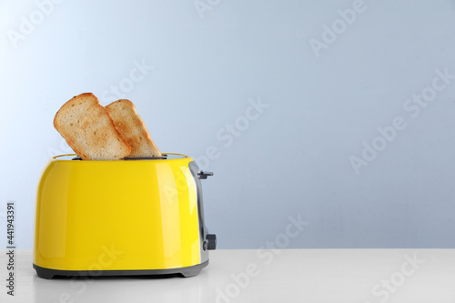 Bread slices popping up out of electric toaster on light table. Space for text